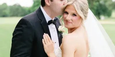 A bride and groom sharing a kiss in a field, with the groom in a black tuxedo and the bride in a white wedding dress.