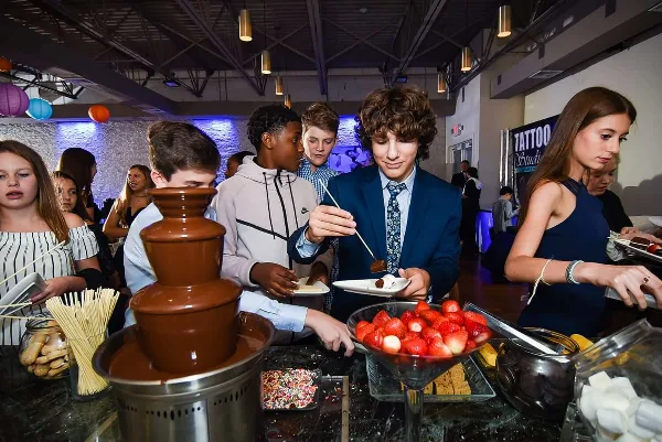 Guests at a social event interacting with a chocolate fountain and dessert station.