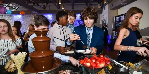 Guests at a social event interacting with a chocolate fountain and dessert station.