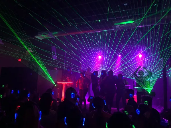 A DJ performing at an event with green laser lights and a crowd dancing.