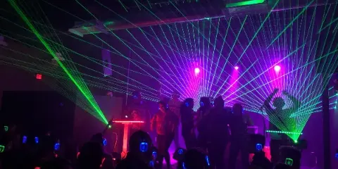 A DJ performing at an event with green laser lights and a crowd dancing.