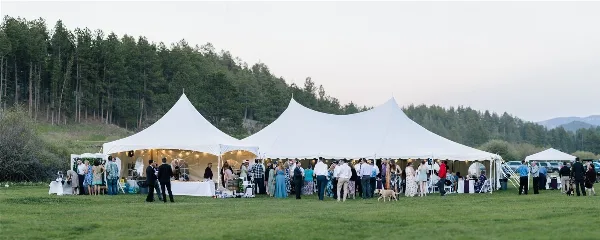 A large white event tent set up in a grassy field with guests gathered around tables and a bar area.