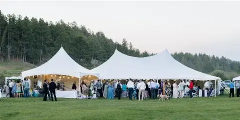A large white event tent set up in a grassy field with guests gathered around tables and a bar area.