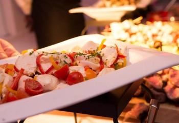 A close-up of a plated seafood dish with tomatoes and herbs being served on a white platter.