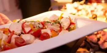 A close-up of a plated seafood dish with tomatoes and herbs being served on a white platter.