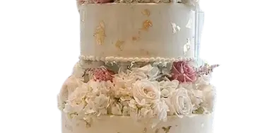A four-tier white wedding cake decorated with fresh roses, gold leaf accents, and a draped fondant base.