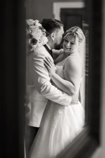 A black and white photograph of a bride and groom embracing and smiling in a wedding dress and suit.