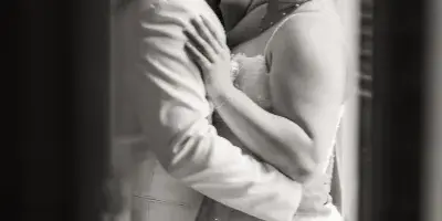 A black and white photograph of a bride and groom embracing and smiling in a wedding dress and suit.