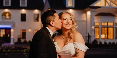 A bride and groom embracing in front of a white estate building at dusk.