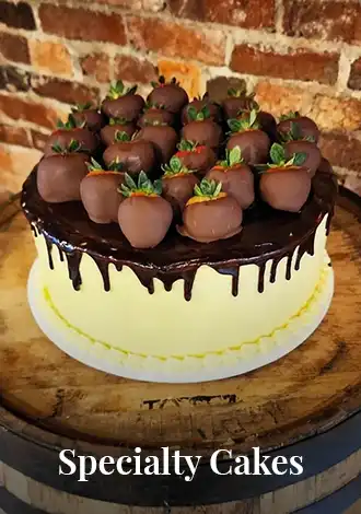 A chocolate-dipped specialty cake topped with chocolate-covered strawberries on a wooden stand.