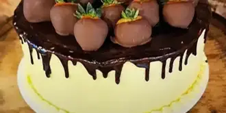 A chocolate-dipped specialty cake topped with chocolate-covered strawberries on a wooden stand.