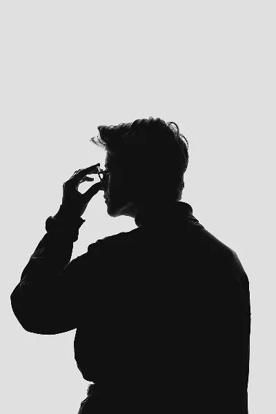 Black-and-white silhouette portrait of a person in profile adjusting glasses against a light background.