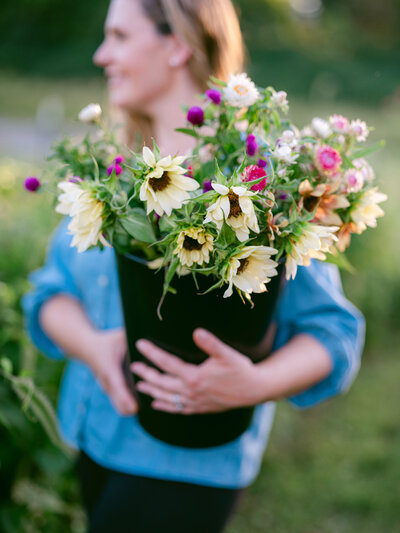 A person holding a bucket of freshly cut flowers including sunflowers and dahlias.