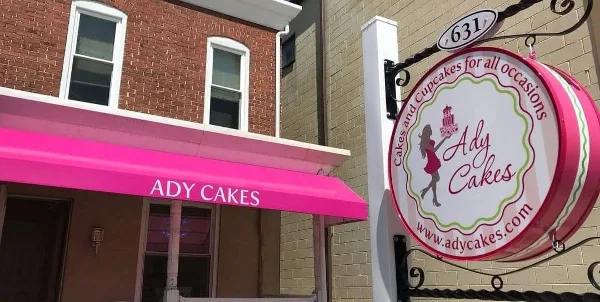Storefront of Ady Cakes with a pink awning and a hanging sign featuring the business logo and website.