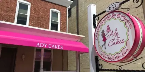 Storefront of Ady Cakes with a pink awning and a hanging sign featuring the business logo and website.