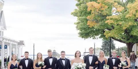 Wedding party posing outdoors with the bride and groom holding white bouquets.