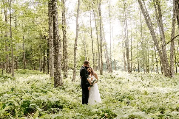 A bride and groom standing together in a lush fern forest clearing with tall trees.