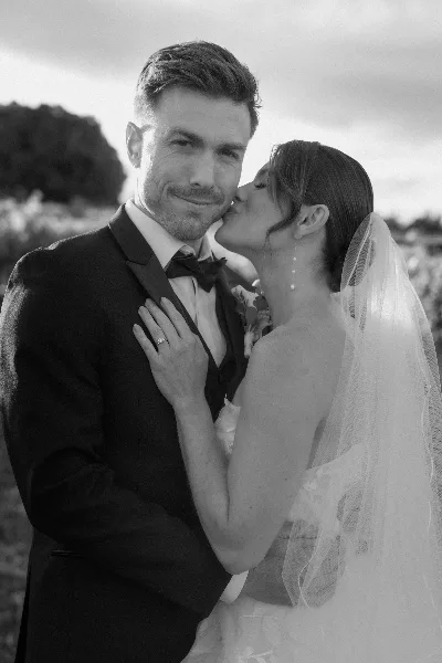 Black and white portrait of a bride kissing a groom on the cheek.