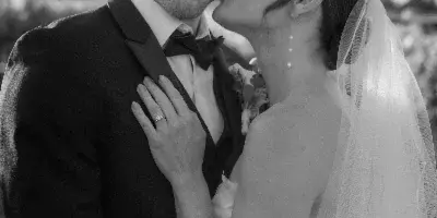 Black and white portrait of a bride kissing a groom on the cheek.