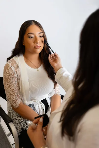 A makeup artist applying makeup to a seated client using a brush.