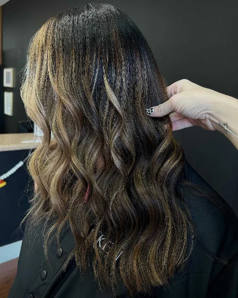 Stylist's hand adjusting a client's wavy, highlighted hair in a salon setting.