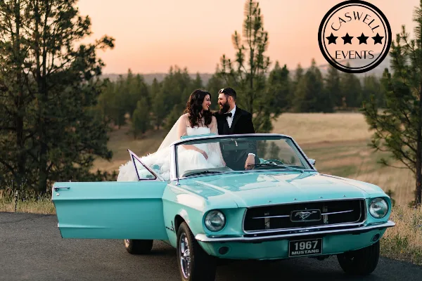A bride and groom posing with a vintage teal 1967 Mustang convertible in a scenic outdoor setting, with the Caswell Events logo in the corner.