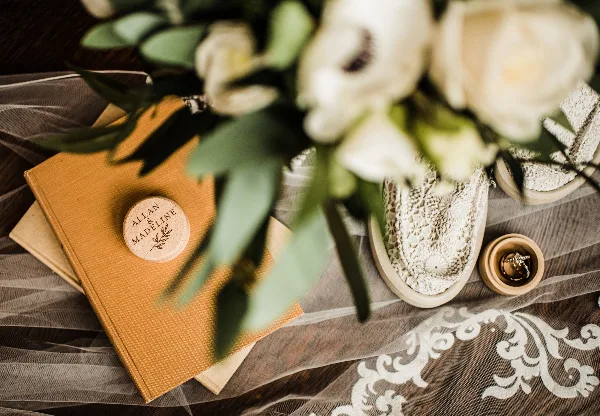 A close-up of a wedding table setting featuring a leather-bound guest book with a wooden seal, white flowers, and lace details.
