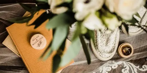 A close-up of a wedding table setting featuring a leather-bound guest book with a wooden seal, white flowers, and lace details.