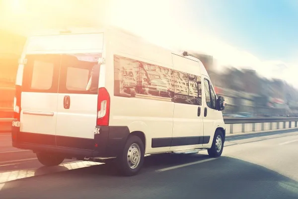 A white passenger van driving on a highway during the day.