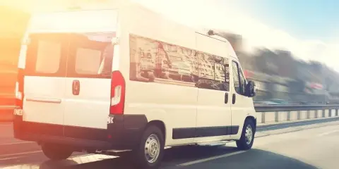 A white passenger van driving on a highway during the day.