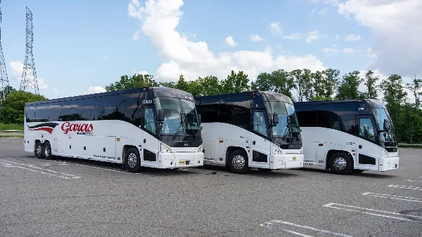 A fleet of white and black charter buses with Garas Transport branding parked in a lot.