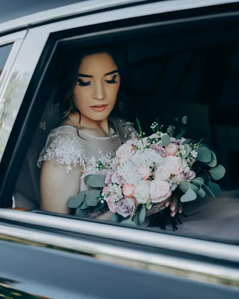 Bride holding a floral bouquet seated inside a car window