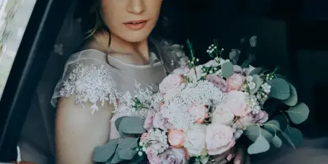 Bride holding a floral bouquet seated inside a car window