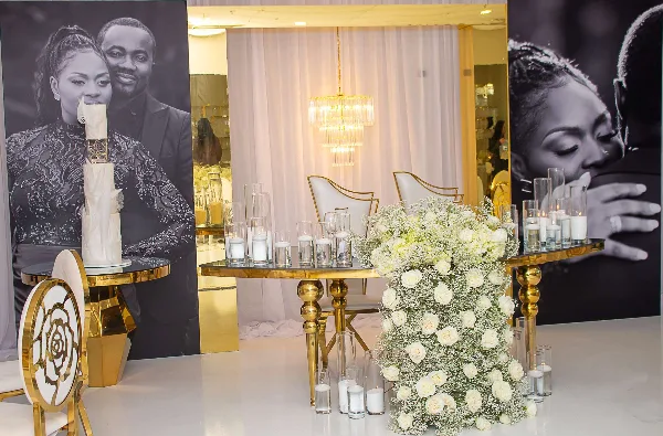 A wedding event setup featuring gold highboy tables, white chairs, and floral centerpieces.