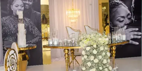 A wedding event setup featuring gold highboy tables, white chairs, and floral centerpieces.
