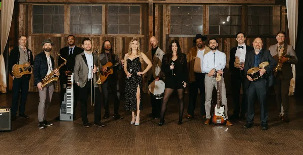 A group of musicians standing in a line holding various instruments including guitars, saxophones, and drums.