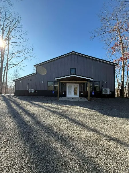 Exterior view of the Kumberland Events Center building, featuring a dark metal roof, a covered entrance, and a gravel parking area.