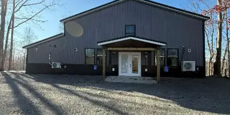 Exterior view of the Kumberland Events Center building, featuring a dark metal roof, a covered entrance, and a gravel parking area.