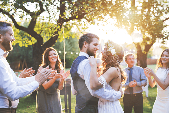 A bride and groom dancing at an outdoor wedding reception while guests applaud.