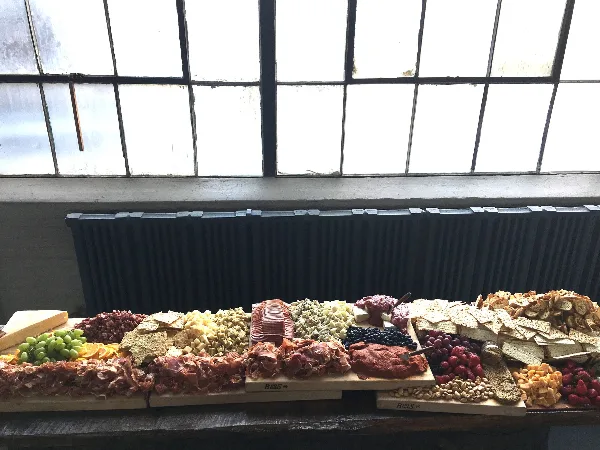 A long table display of charcuterie, cheeses, crackers, nuts, and fresh fruit arranged for a catering event.