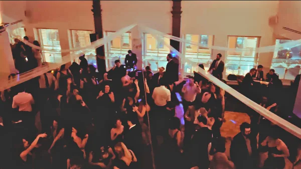 A crowded dance floor at a wedding event with a DJ at the booth and guests dancing.