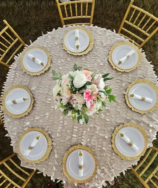 An overhead view of an elegant outdoor wedding table setting featuring gold Chiavari chairs, white and gold plates, and a lush floral centerpiece.