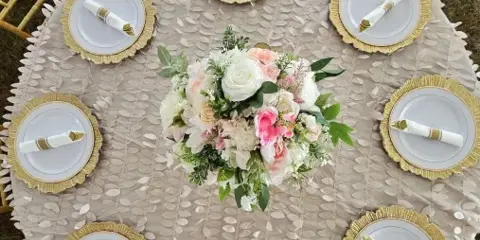 An overhead view of an elegant outdoor wedding table setting featuring gold Chiavari chairs, white and gold plates, and a lush floral centerpiece.