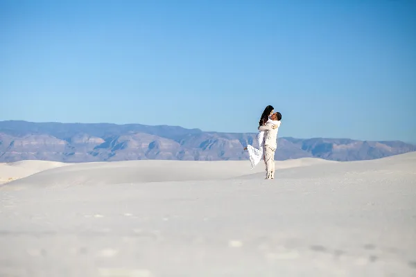 A couple embracing in a white sand dune landscape with mountains in the background.