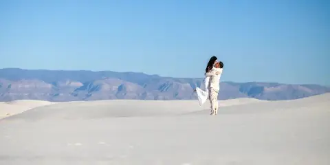A couple embracing in a white sand dune landscape with mountains in the background.