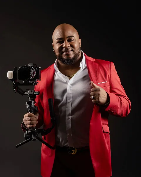 A man in a red blazer holding a professional Sony video camera on a gimbal stabilizer.