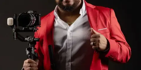 A man in a red blazer holding a professional Sony video camera on a gimbal stabilizer.