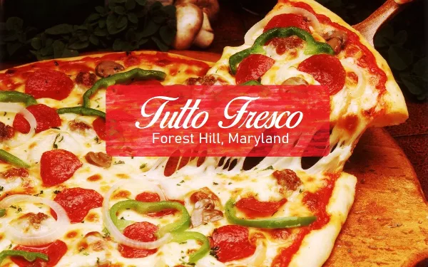 A whole Italian pizza with pepperoni, green peppers, onions, and mushrooms on a wooden board with a slice being lifted.