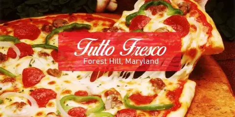 A whole Italian pizza with pepperoni, green peppers, onions, and mushrooms on a wooden board with a slice being lifted.