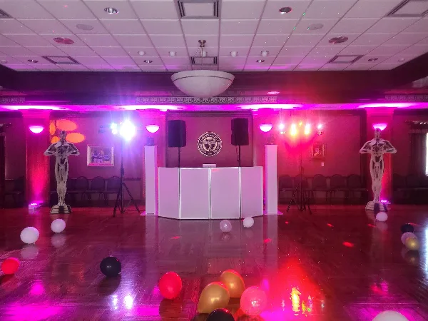 A dance floor with a white DJ booth, black speakers, and colorful stage lighting in a ballroom.